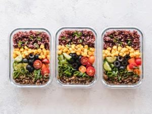 Three meal prep containers with grains, lentils, and vegetables